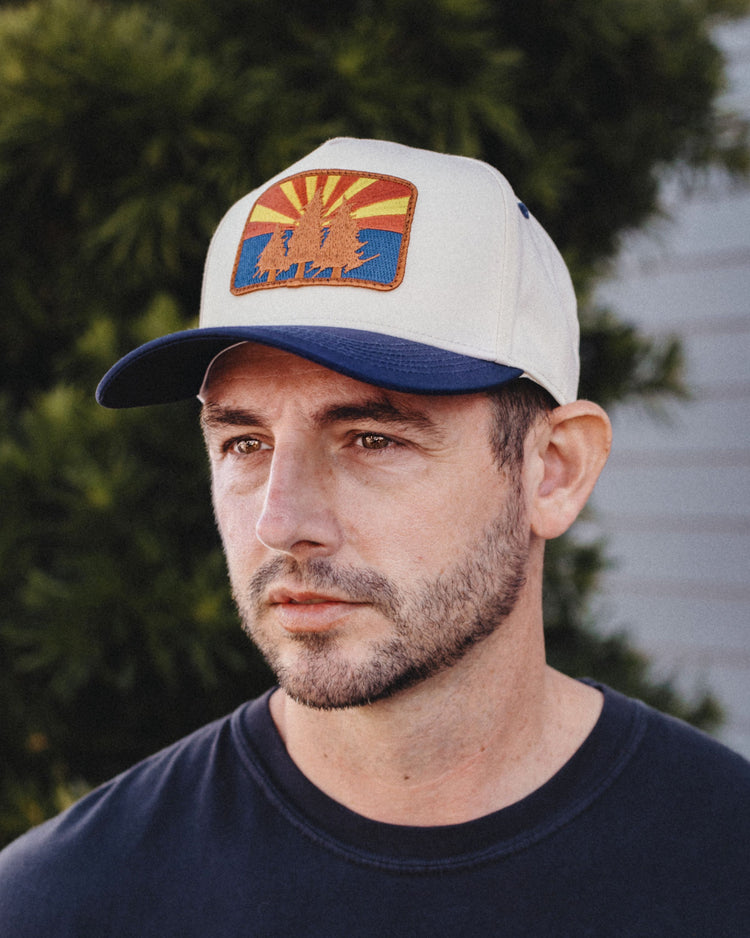 Man wearing the cream and navy AZ Pines Two Tone Hat with an Arizona flag pine tree patch