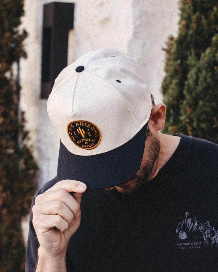 Man looking down in the cream and black The Shop Two Tone Hat with a gold and black Ramble and Roam patch