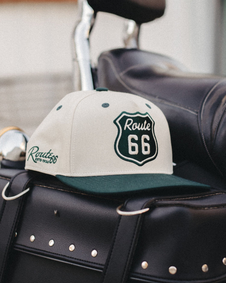 Cream and green Route 66 Road Sign Two Tone Hat resting on a black leather motorcycle seat