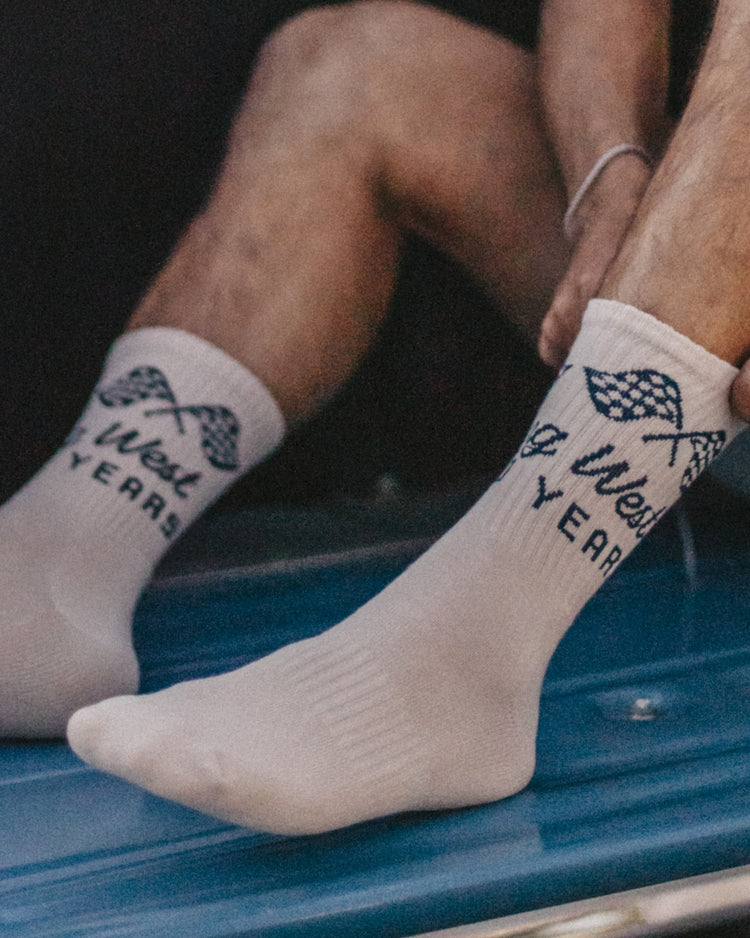 Close-up of white Heading West for 100 Years crew socks with checkered flags on a blue truck bed